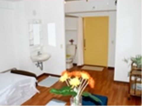 壁際に低床型のベッドがあり、その隣に正面に鏡と収納棚がある洗面台がある。壁を隔てて温水洗浄便座が置かれている。