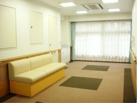 奥が一面ガラス戸で、引かれたレースカーテンが白く光っている。壁には手すりがあり、その下に３人掛けのソファが置かれている。