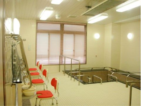 Ｌ字型の広い浴槽がある浴室。湯は張られていない。浴槽を囲むように多数の手すりが設置されており、安全に入浴できる。