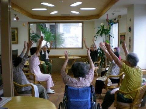 椅子に座って円形に並び、スタッフの指導のもとで体操をする入居者様