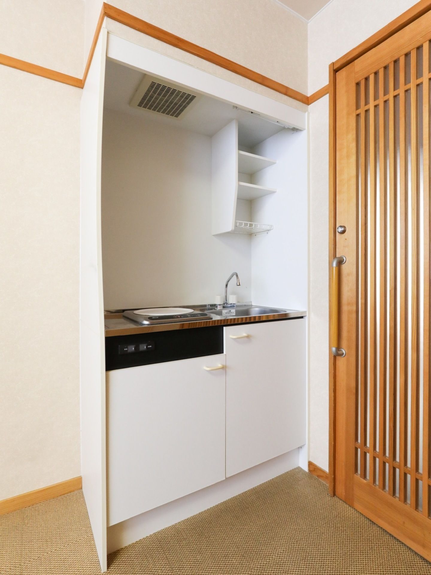 入口ドアのすぐ横にシンク、換気扇、IHヒーター、上下に棚が付いているミニキッチンが備え付けられている。