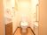 個室全体が茶と白でコーディネートされたトイレである。壁面に縦横に取り付けられた手すりも茶色である。洗面台が個室内にある。