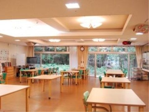 食堂にはテーブル、緑色の背もたれがある椅子が並べられている。大きな窓があり、外には木や草が広がった景色が見える。