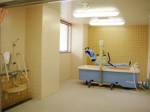 窓のついた明るい浴室。寝たままの姿勢で入浴できるストレッチャー付きの青いバスタブが、壁沿いに置かれている。