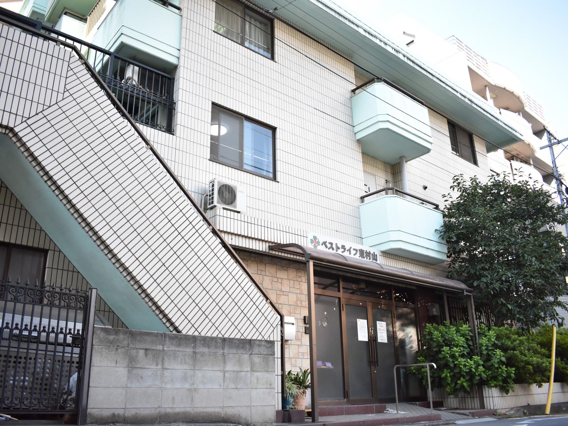 大きなマンションのような外観。各部屋にバルコニーがついている。入り口前には屋根のついた休憩所が設置されている。