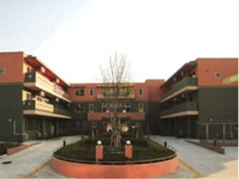 中央に丸い植え込みがある３階建ての建物は、外壁がレンガ色と緑色のツートーンに塗られている。２，３階にはベランダがある。