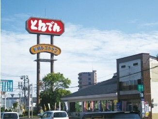 三角の屋根の建物の前に建つ、ファミリーレストランの赤い看板