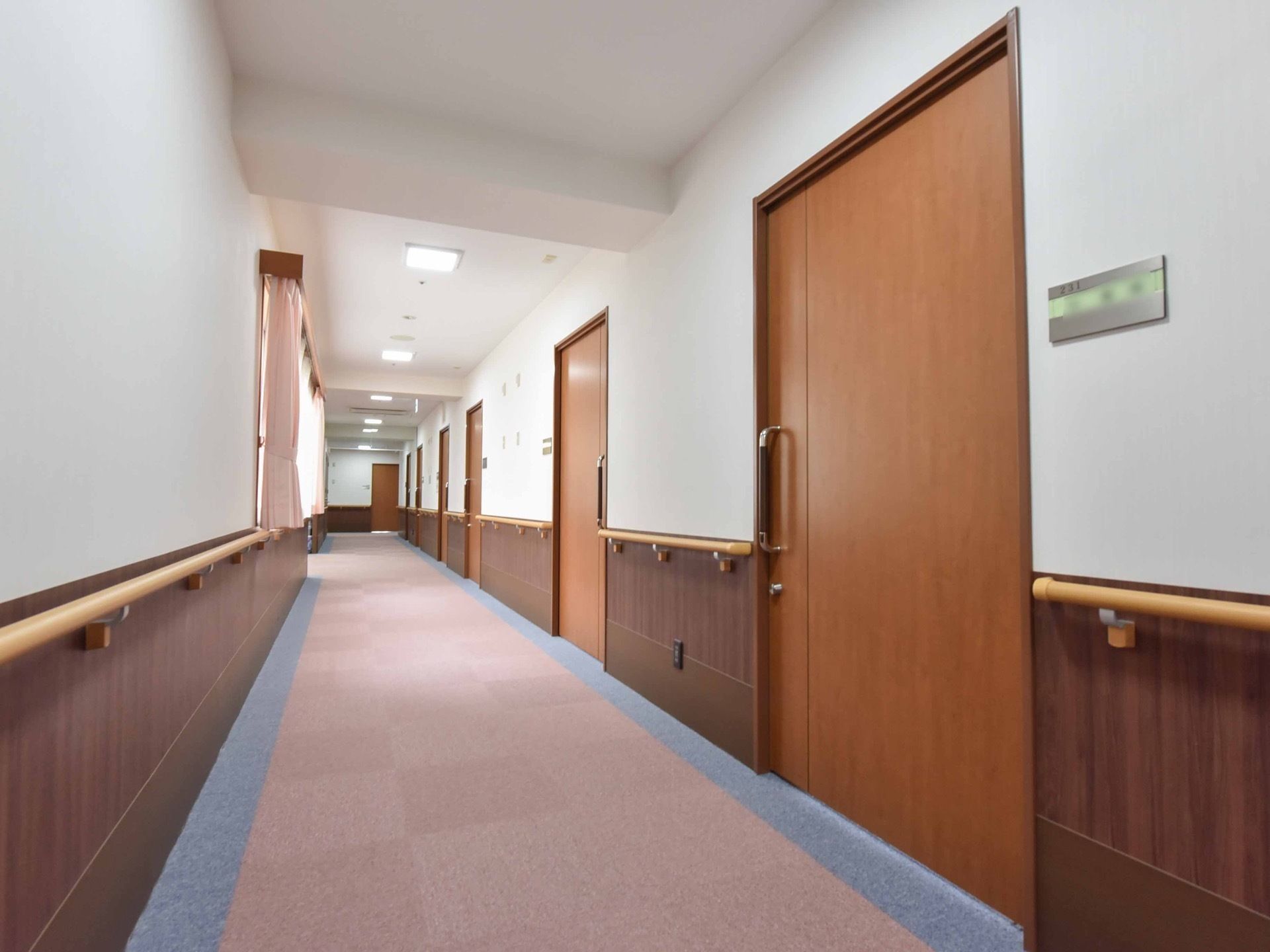 廊下には居室の扉が並んでいる。大きな木目のスライド式になっており、安全に開閉することができる。窓から光が入る明るい空間である。