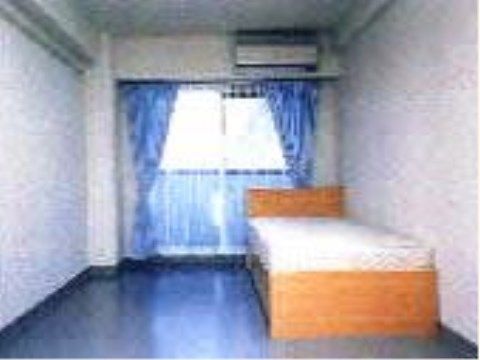 すっきりとした室内に、ベッドが置かれている。広い掃き出し窓があり、青色のカーテンがかかっている。エアコンが備わっている。