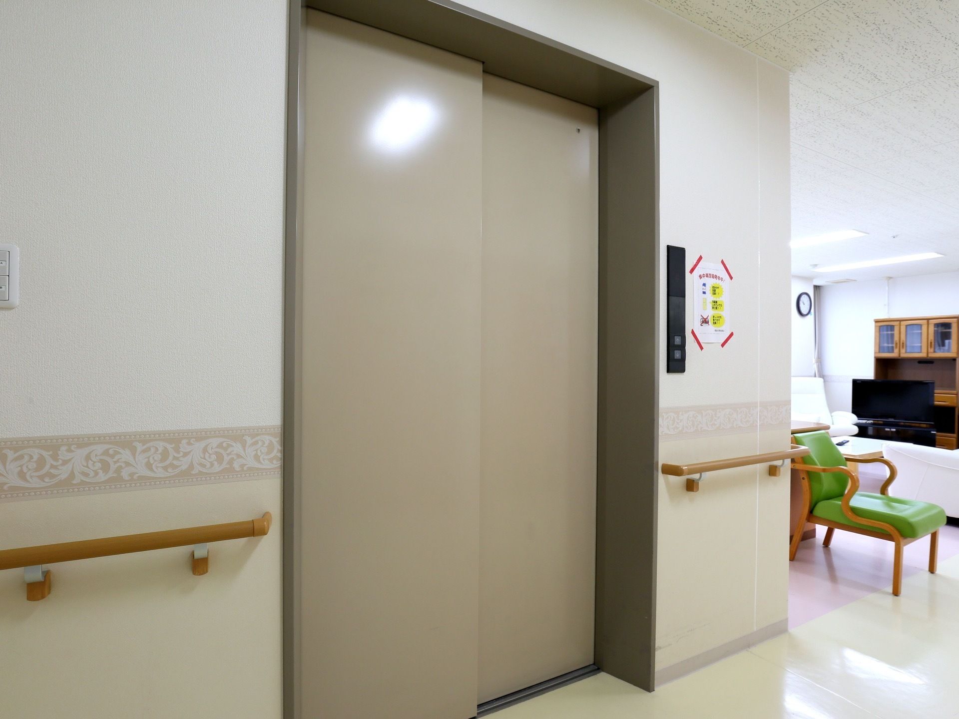 ラウンジの隣に設けられた、グレー色のドアを持つエレベーターである。横の壁に沿って、手すりが設置されている。