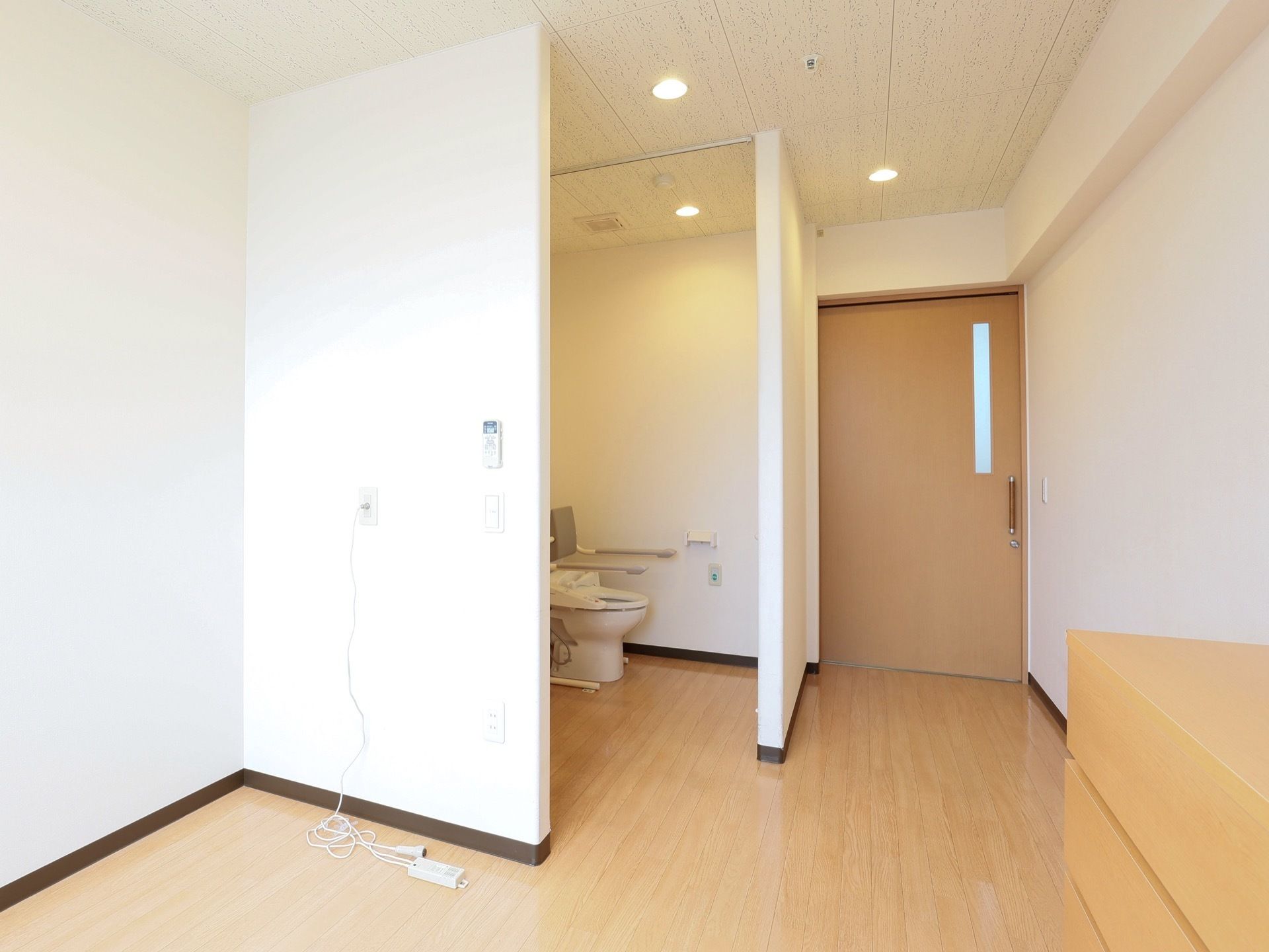 天井、壁は白く、清潔感がある。ドアなしのトイレが設置されている。部屋入り口のドアは、スライド式となっている。