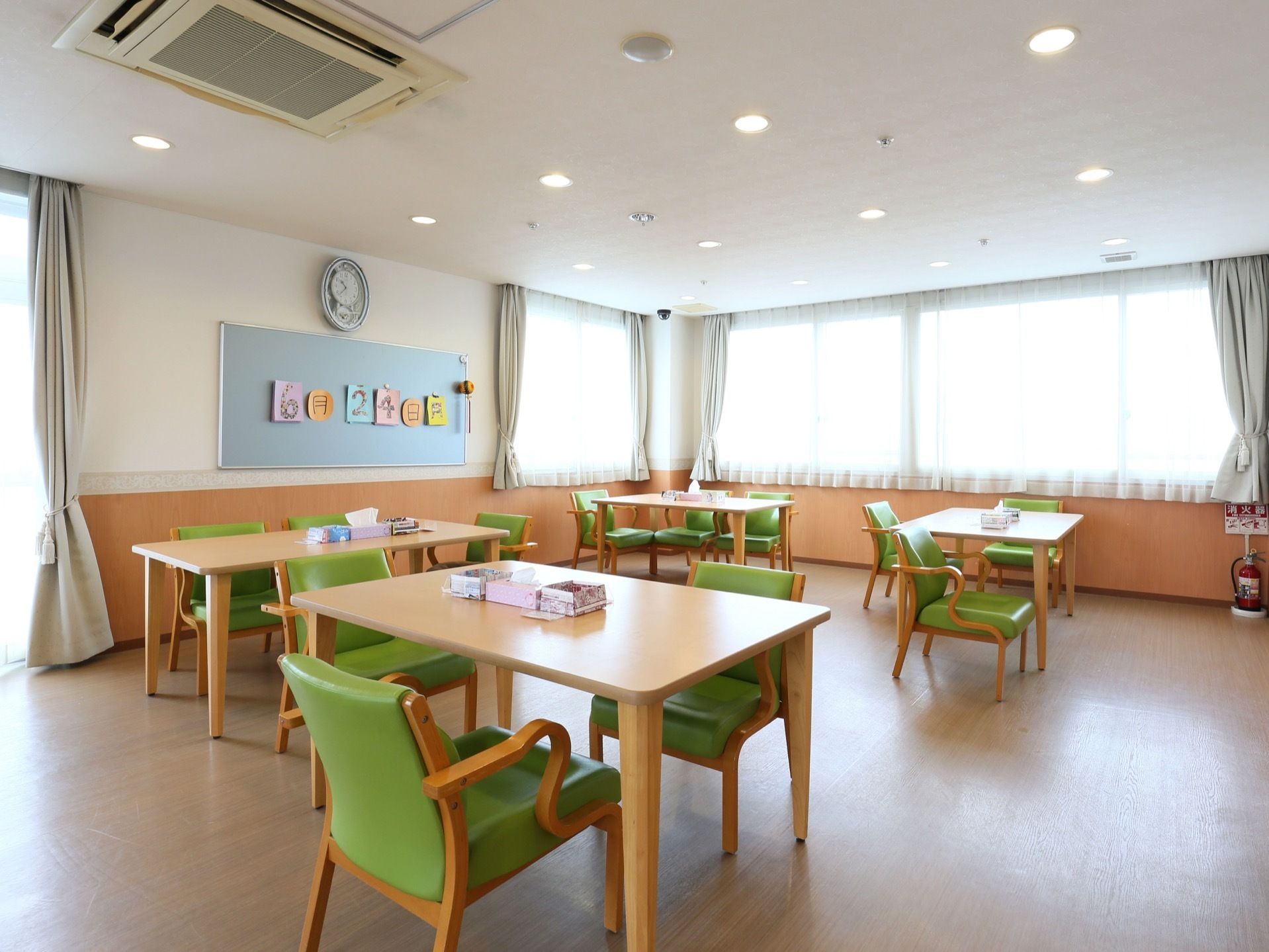 窓からの日差しで明るい部屋である。木製のテーブルと椅子が数組配置されている。正面にホワイトボードがある。