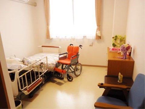 オレンジ色の車椅子がベッドの横に置かれている１人用居室