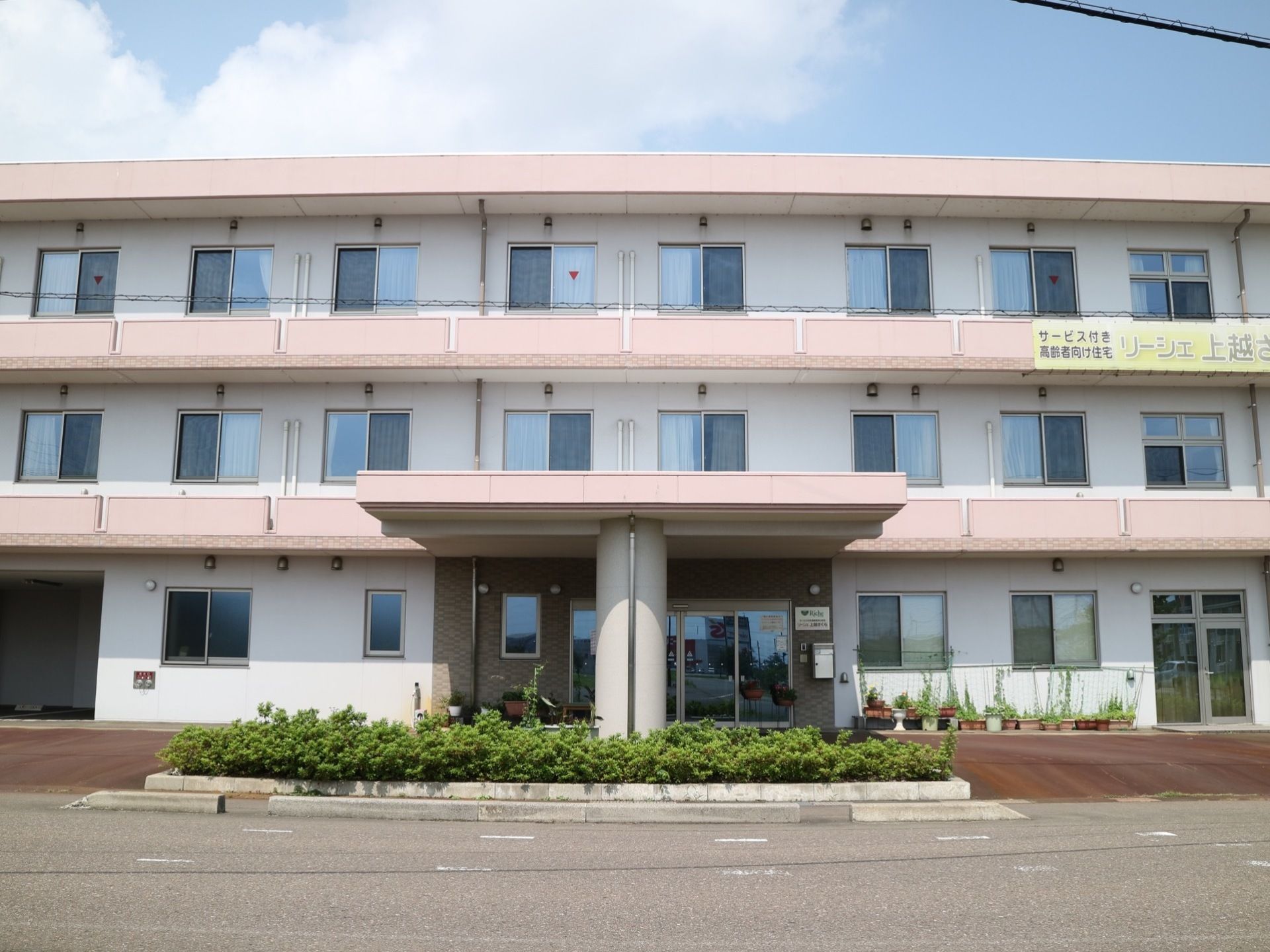 ３階建ての白を基調とした外観である。入口の前に造られた柱が特徴的で、左奥には駐車スペースが設けられている。