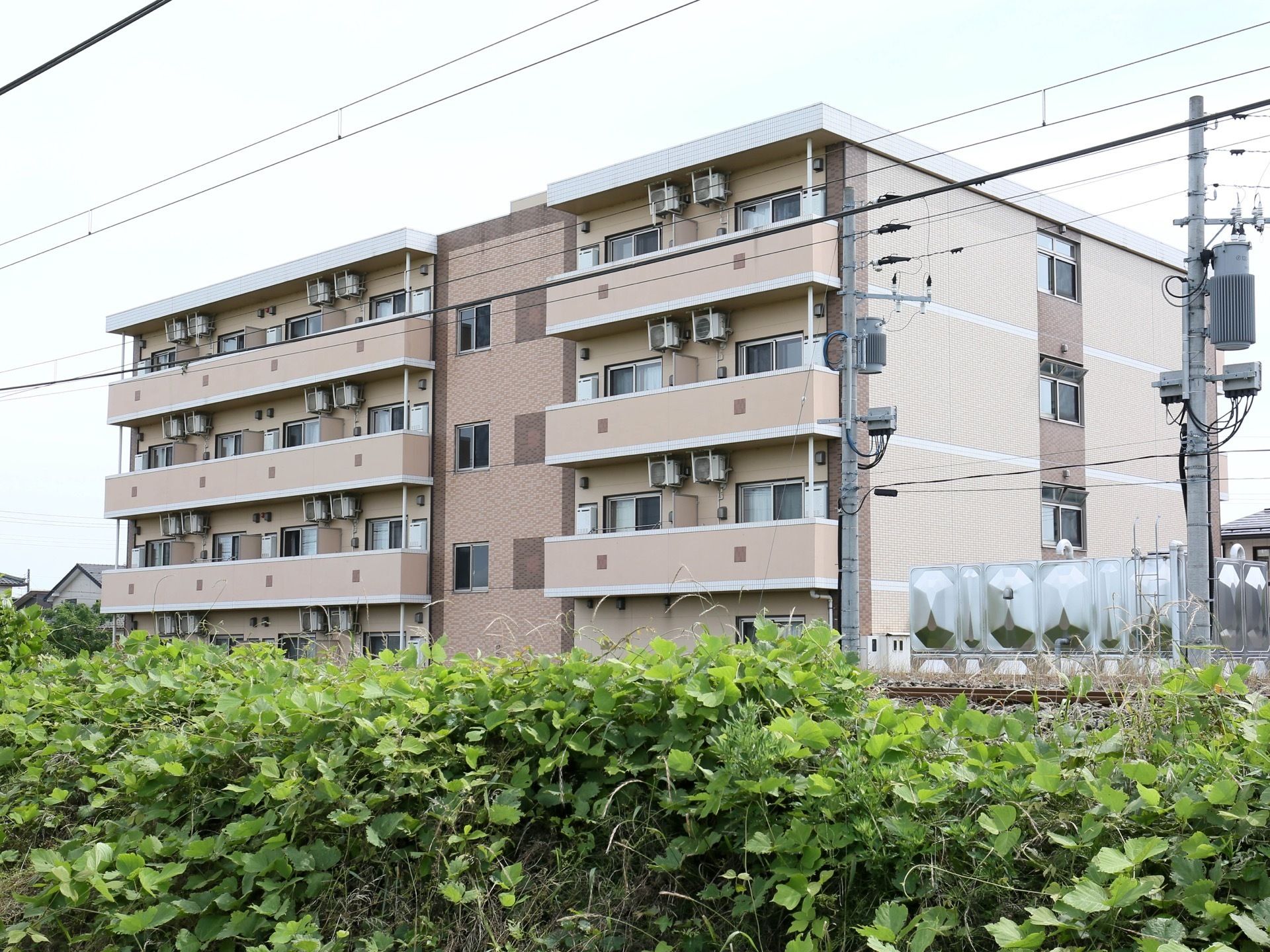 線路脇の敷地にクリーム色の外壁の4階建てマンションが建っている。各階の部屋にはバルコニーがついている。
