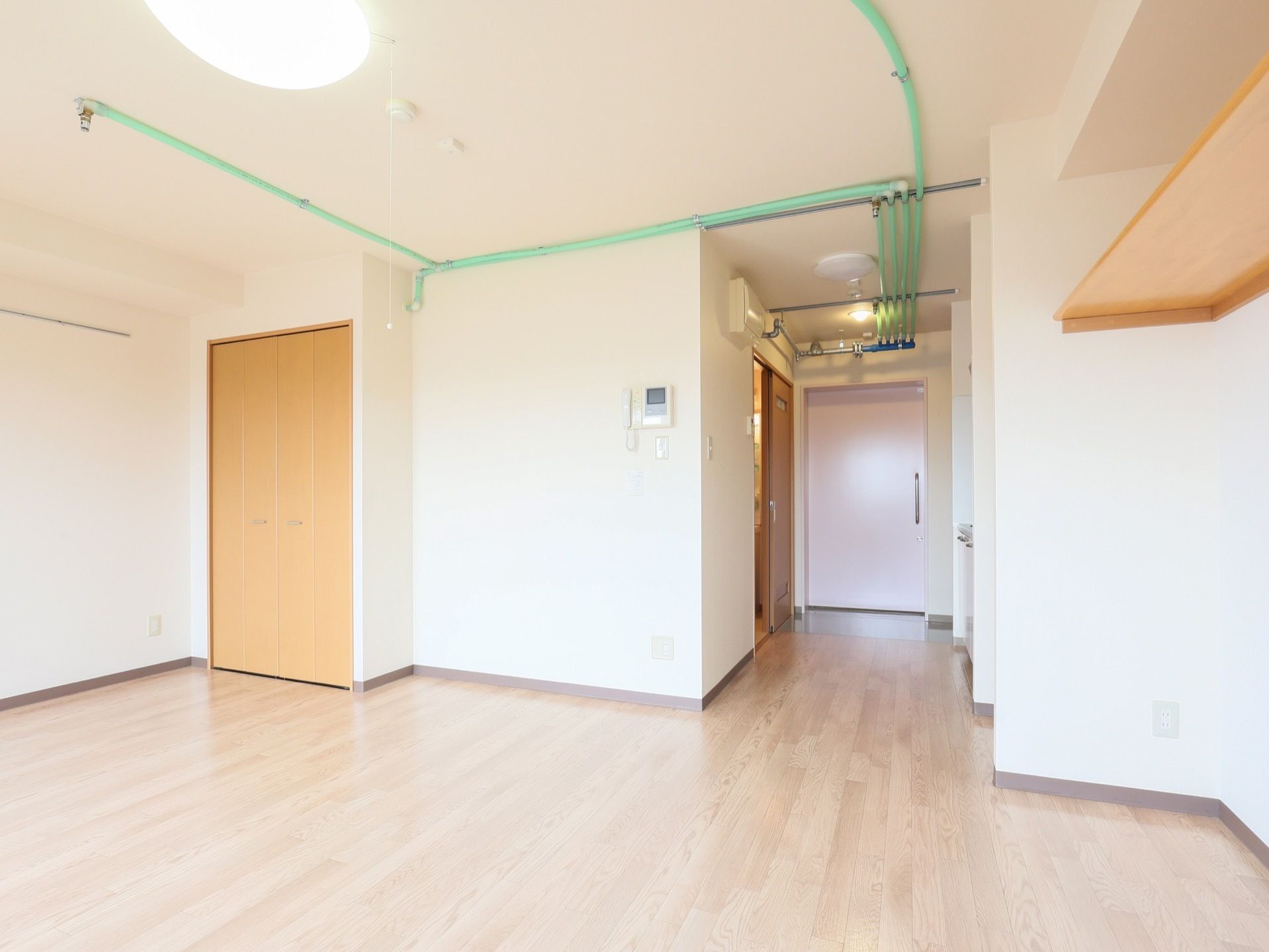 明るいフローリングの居室があり、天井にはスプリンクラー設備の配管が伸びている。壁には収納が備え付けられている。