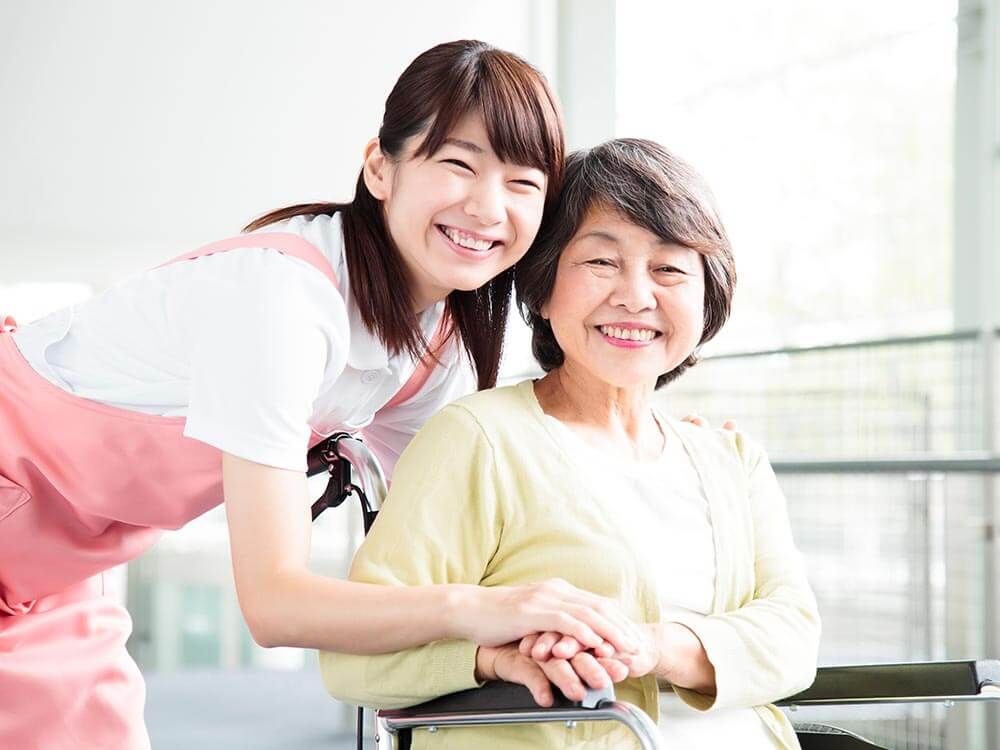青いチェックのパジャマを来た女性入居者様を介助するスタッフ