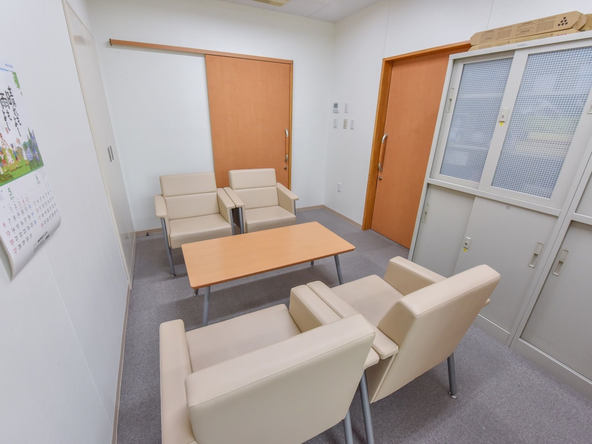 面談スペースには１人掛けのソファが２脚ずつ、テーブルをはさんで置かれている。壁にはカレンダーがかけられている。