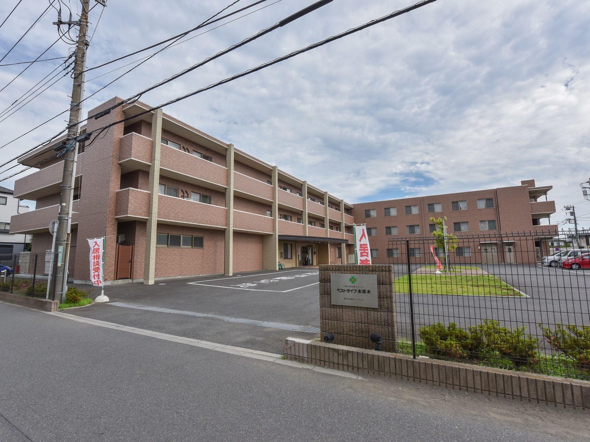 施設入口の門は大きく開いている。施設はフェンスで囲まれており、門に施設名の掛かれた看板が設置されている。