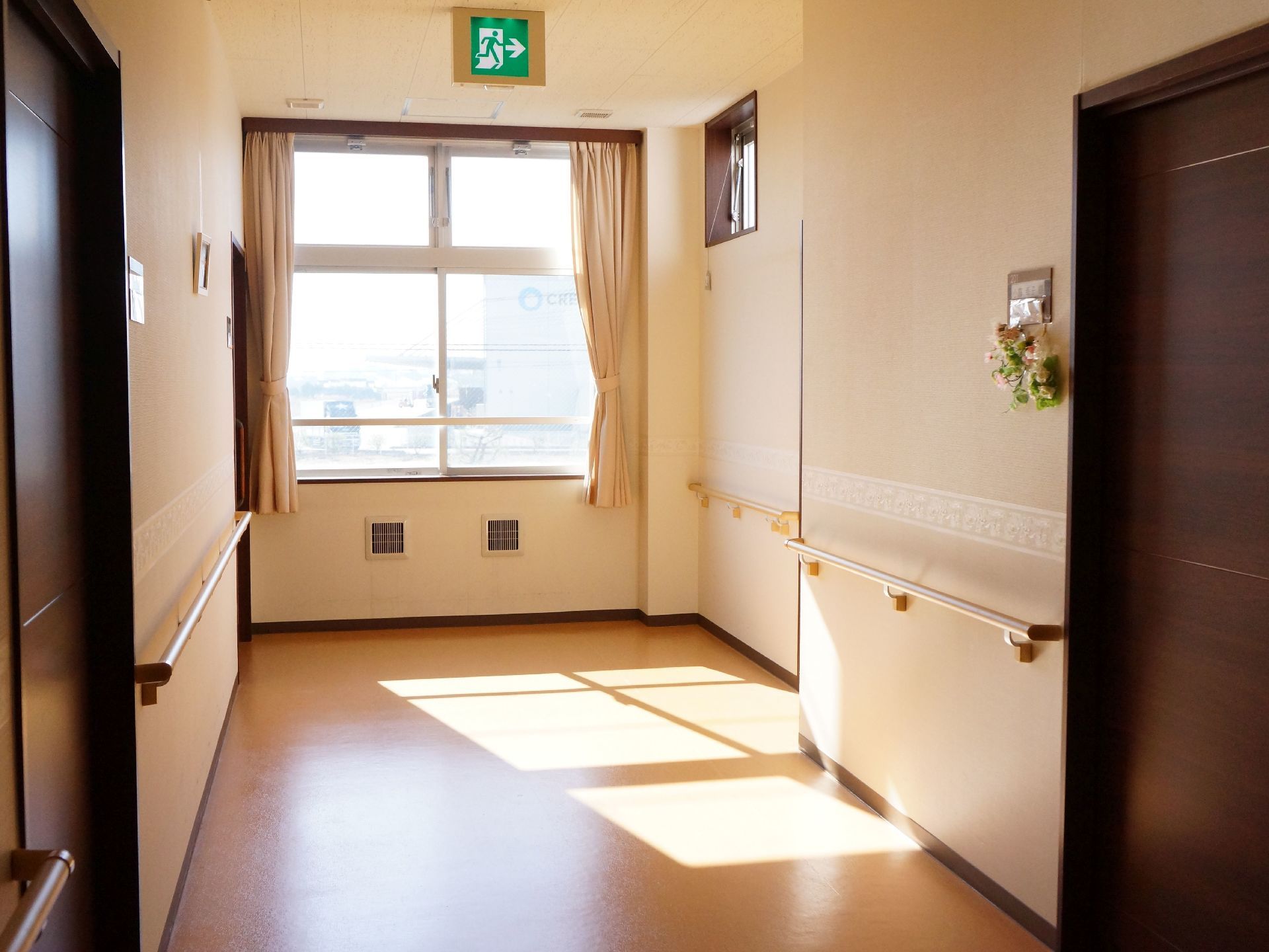通路の奥には大きな窓があり、カーテンが取り付けられている。また天井には非常口への誘導灯を備え付けている。