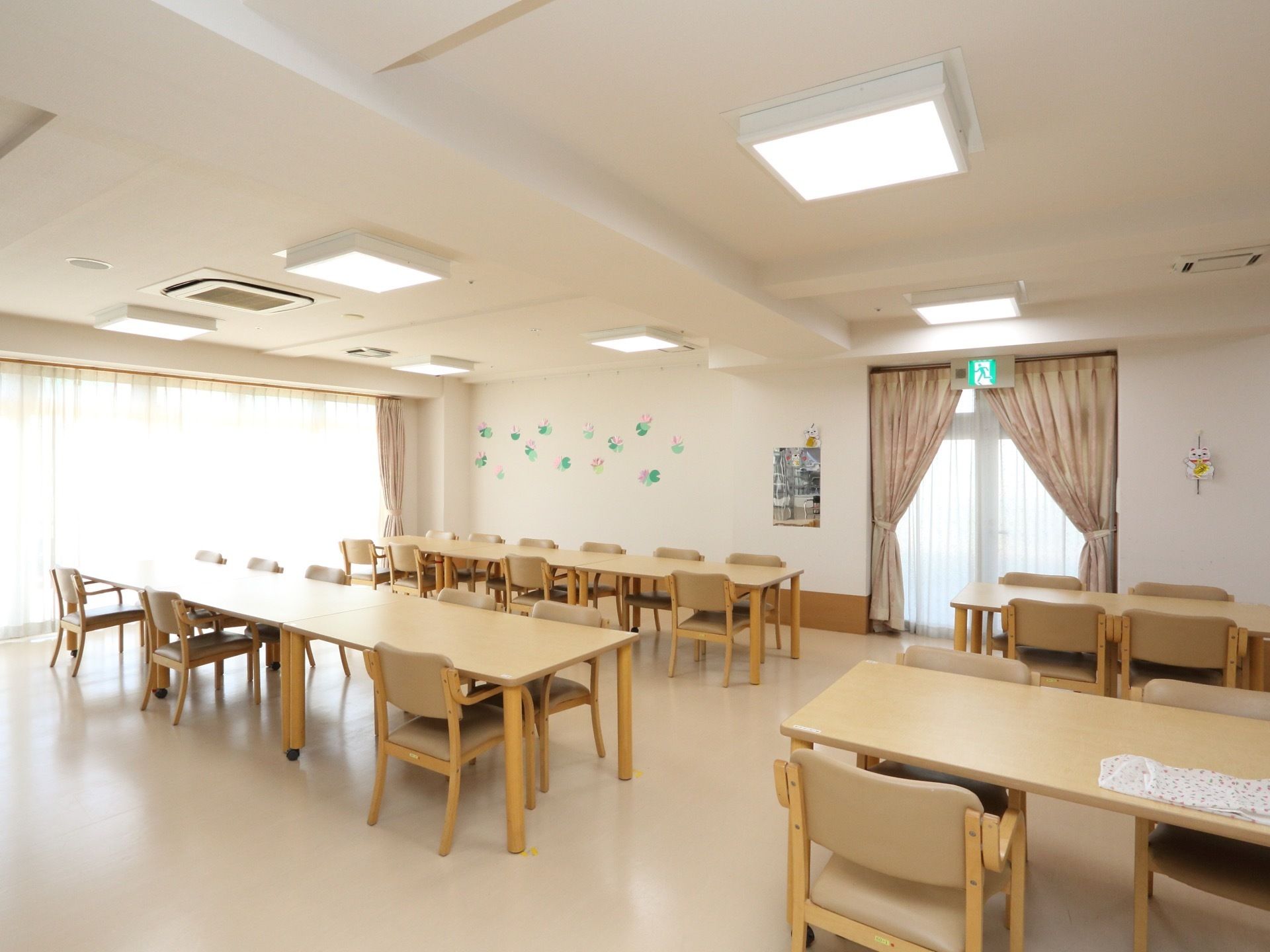 クリーム色の４人掛けテーブルが11台ほど用意されている。また、大きな掃き出し窓から気持ちよく日光が差し込んでいる。