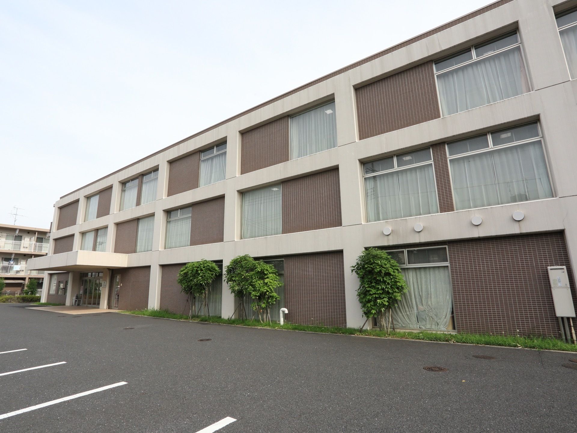 植栽が所々にある広い駐車場が隣接している３階建ての建物
