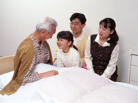 ベッドの上に身を起こした高齢男性と親密に話をする親子