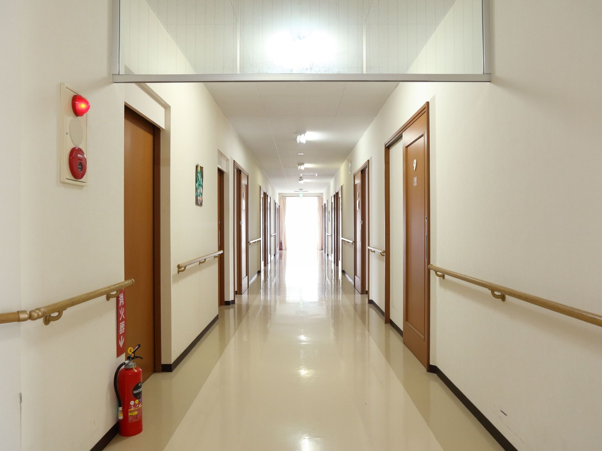 白い壁にクリーム色の床である。長い通路の両側に各居室へ入る木目調の扉がある。各居室の壁には手すりが設置されている。