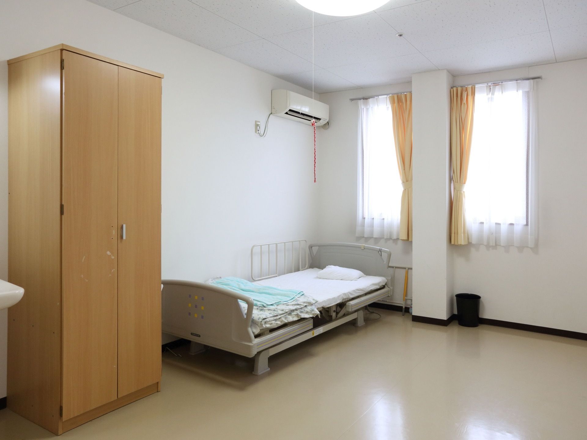 明るい居室の窓際には電動の介護ベッドが設置されており、入居者様は楽に起き上がることができる。エアコン、ロッカーもある。