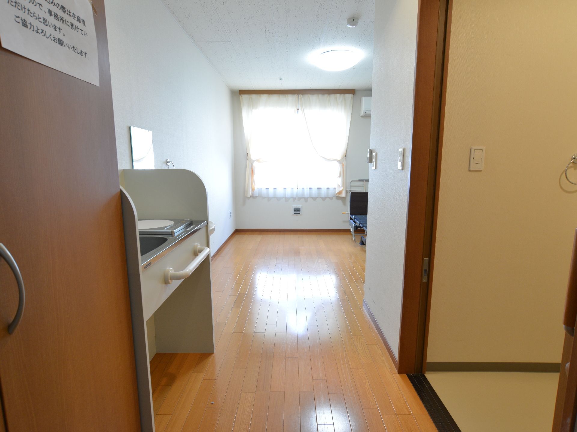 突き当たりの窓からは明るい光が差し込みフローリングの床を照らしている。左側には木目調で両開きの扉も見える。