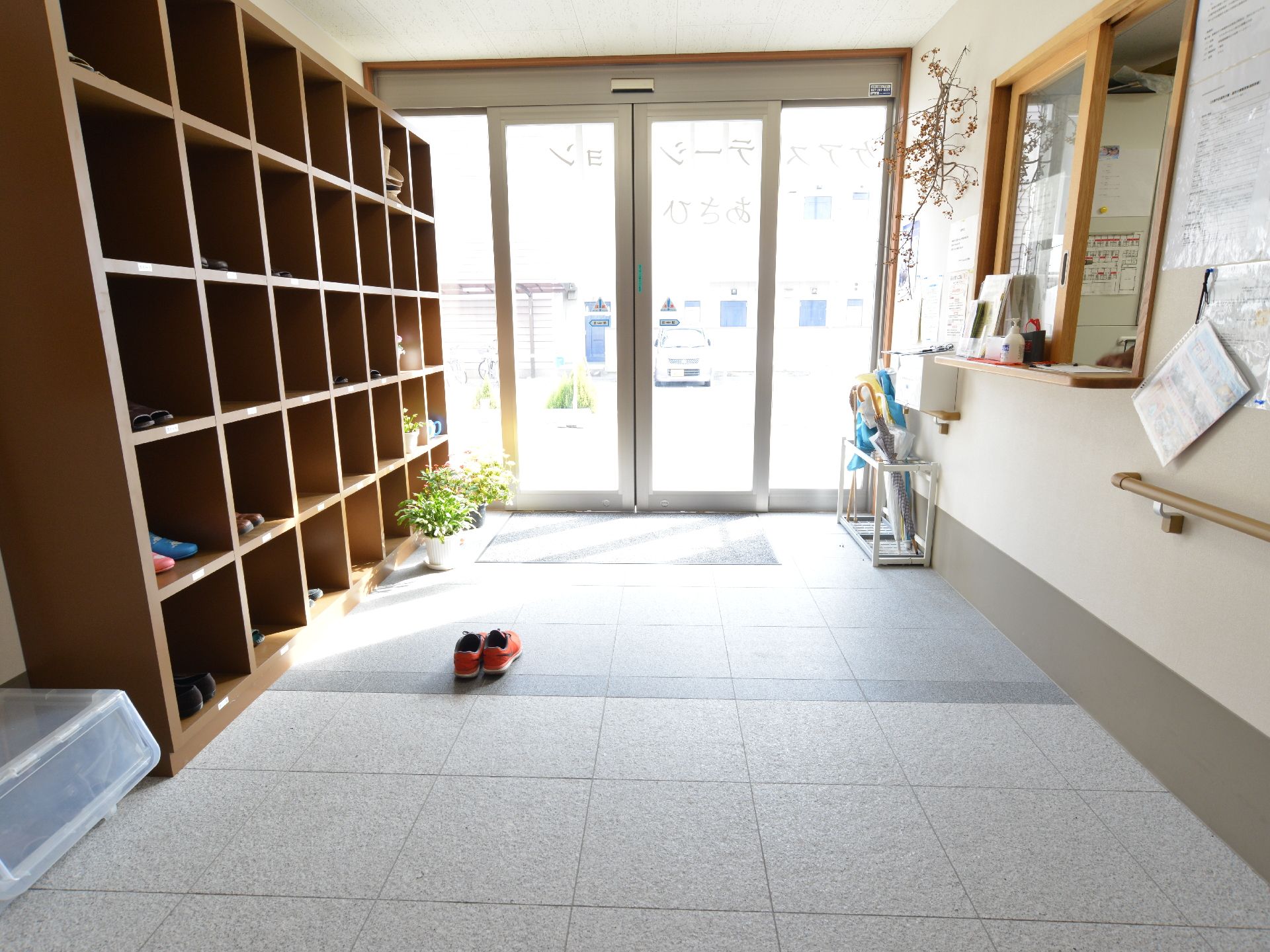 左側には下駄箱があり外と屋内はバリアフリーでつながっている。両開きの自動ドアはガラス製になっており右手には手すりもついている。