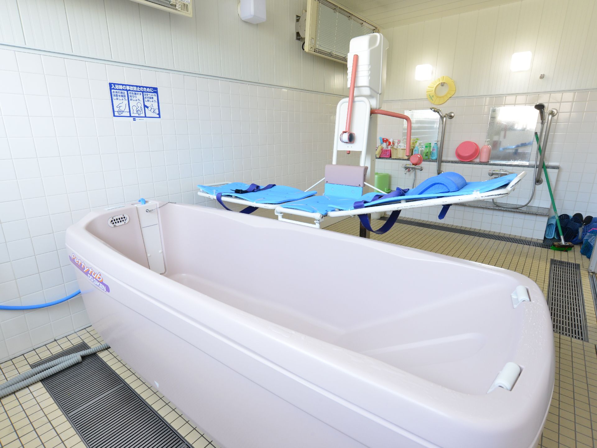 入浴を助ける介護専用器具が2種類置いてある。タイル状の床には排水溝もあり奥には鏡とシャワーが設置されている。
