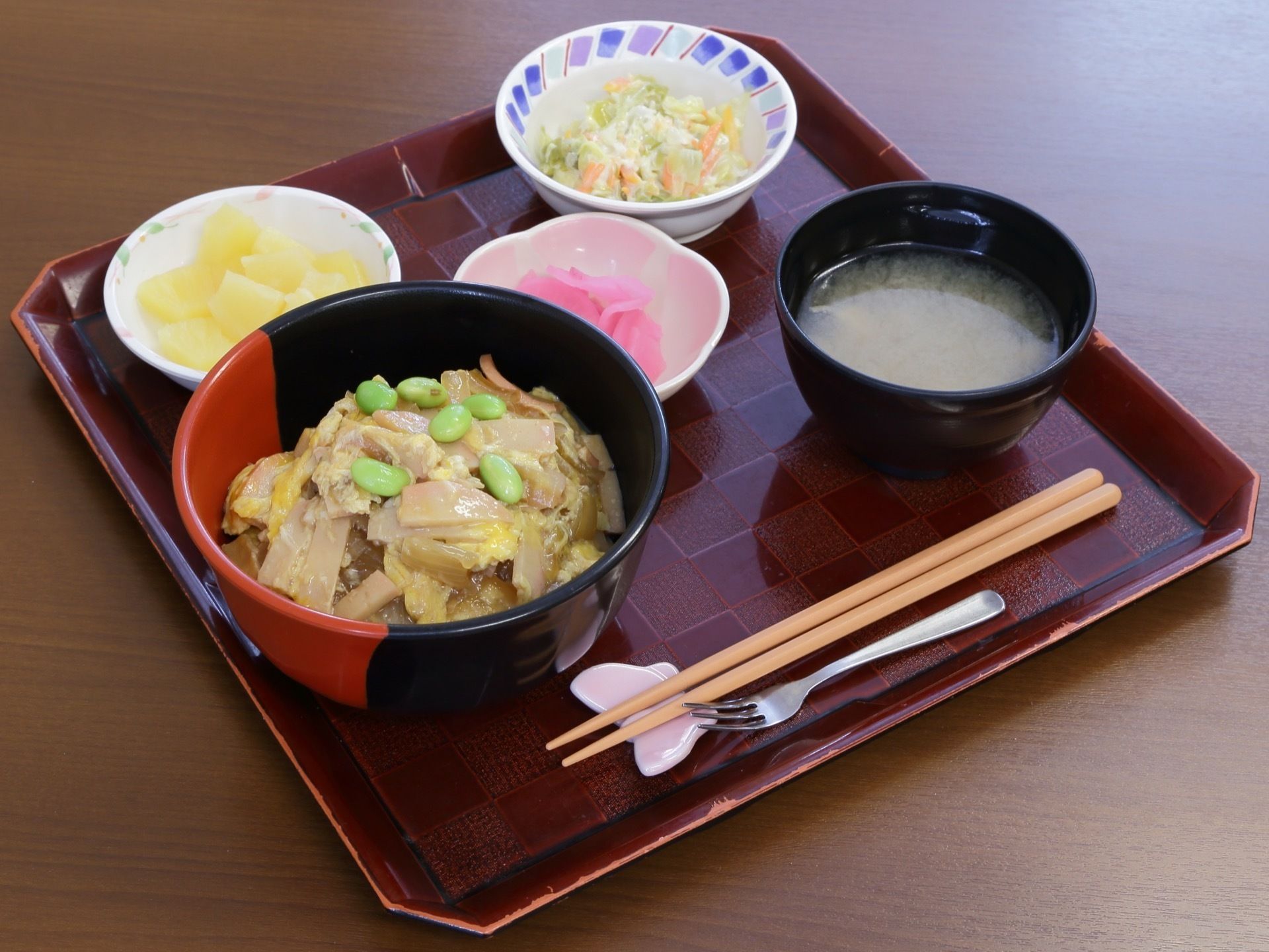 丼ものをメインに、汁物、漬物、副菜、デザートがある。白いちょうちょの箸置きを使っている。色鮮やかな食事となっている。
