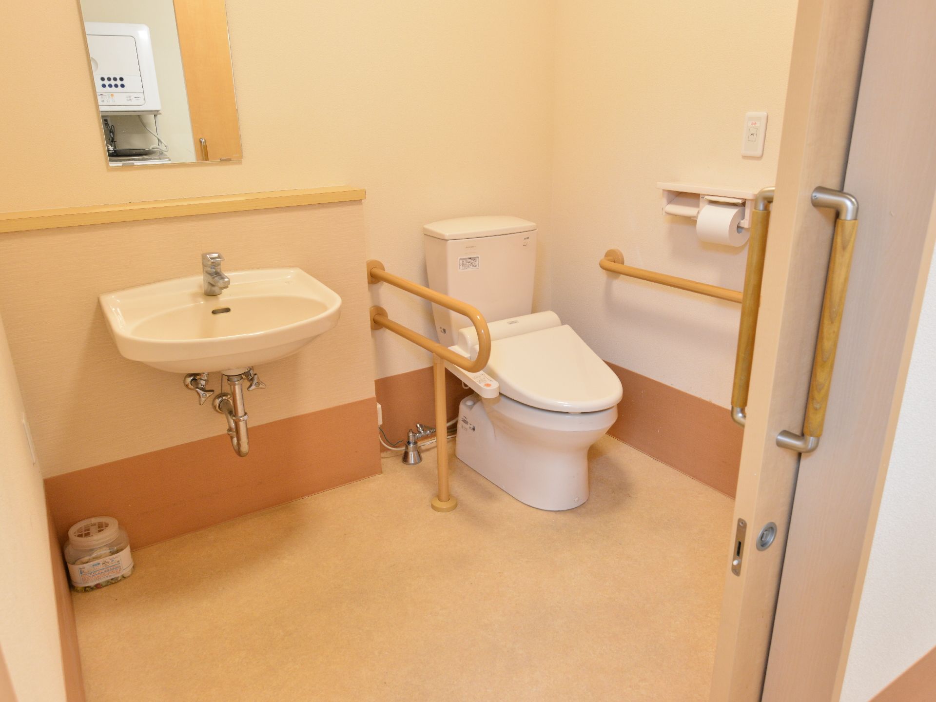 手洗い場と一緒になっているタイプのトイレがある。扉は横開きになっていて、トイレの両脇に手すりがついている。