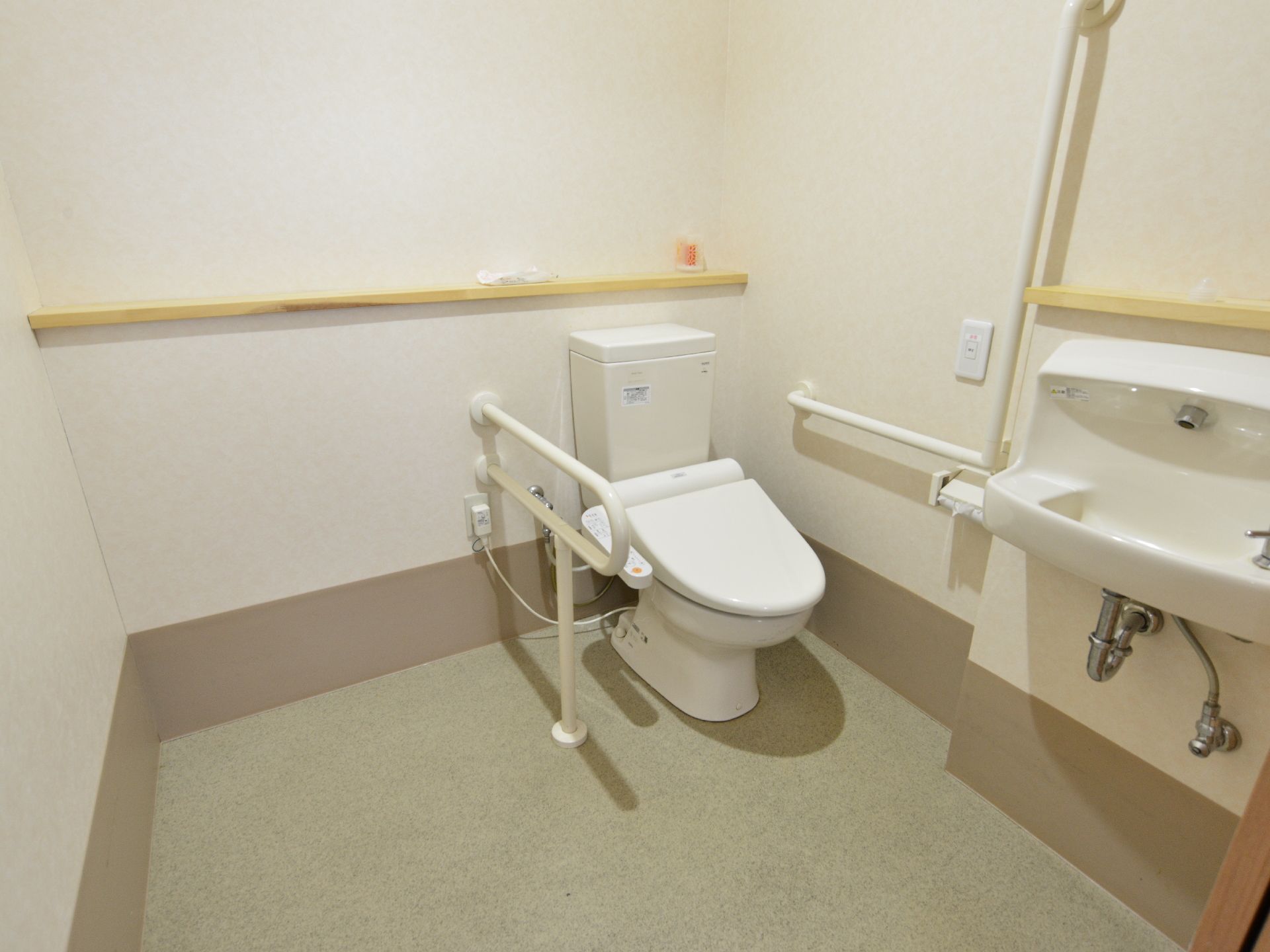 ウォシュレット付きの洋式トイレには、立ち座りを補助してくれる手すりが付いている。洗面台も設置されている。