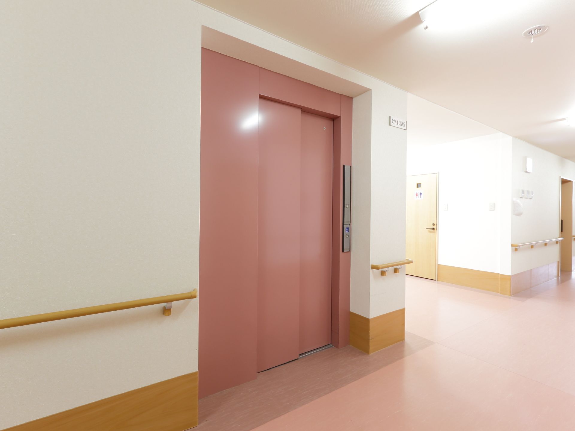 施設は床がピンク色である。エレベーターが設けられており、床よりも濃いピンク色である。壁には手すりが設けられている。
