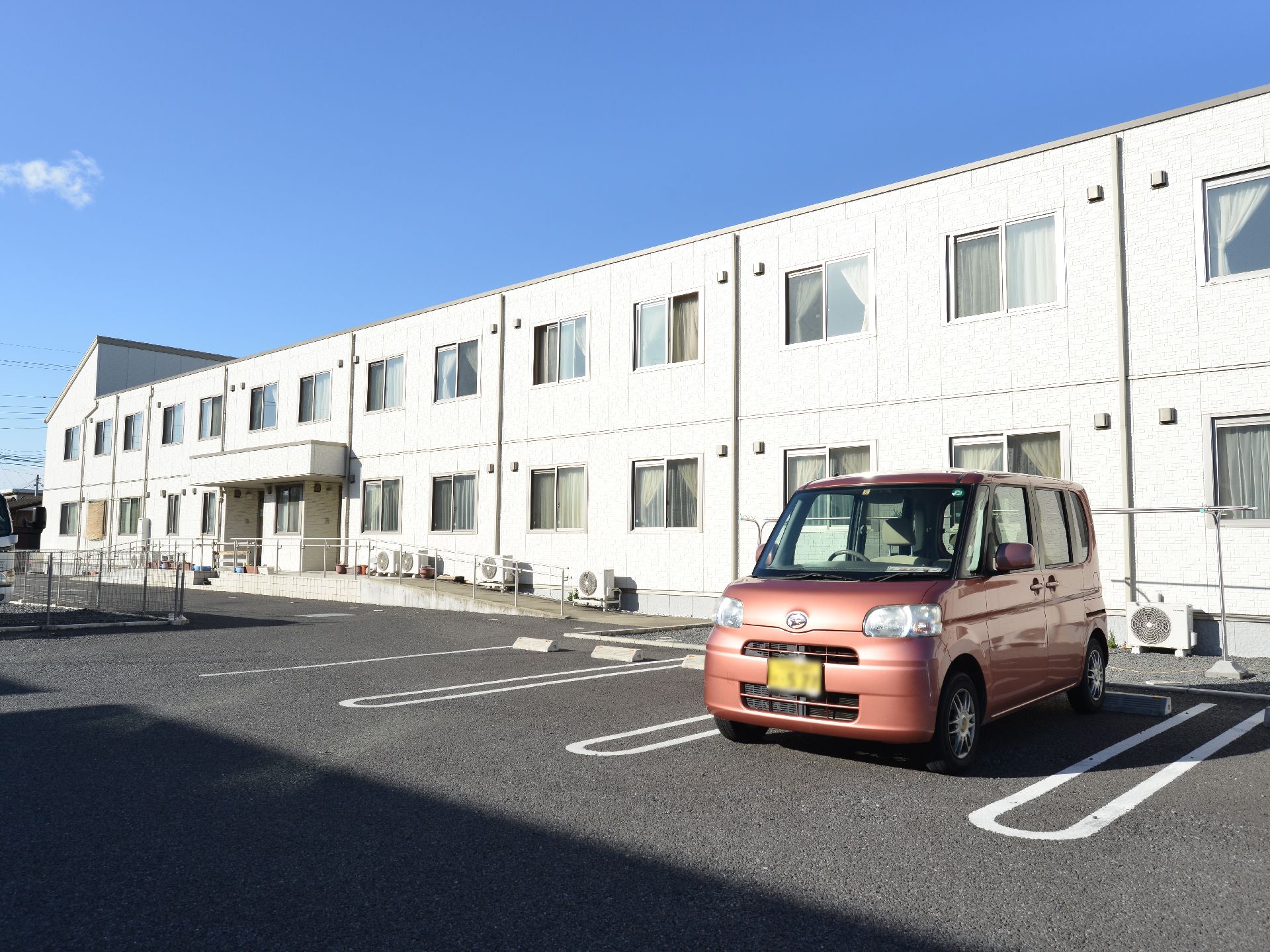 数多く設けられた駐車スペースにハイツのような2階建ての建物である。非常階段や玄関前のスロープなども設置されている。