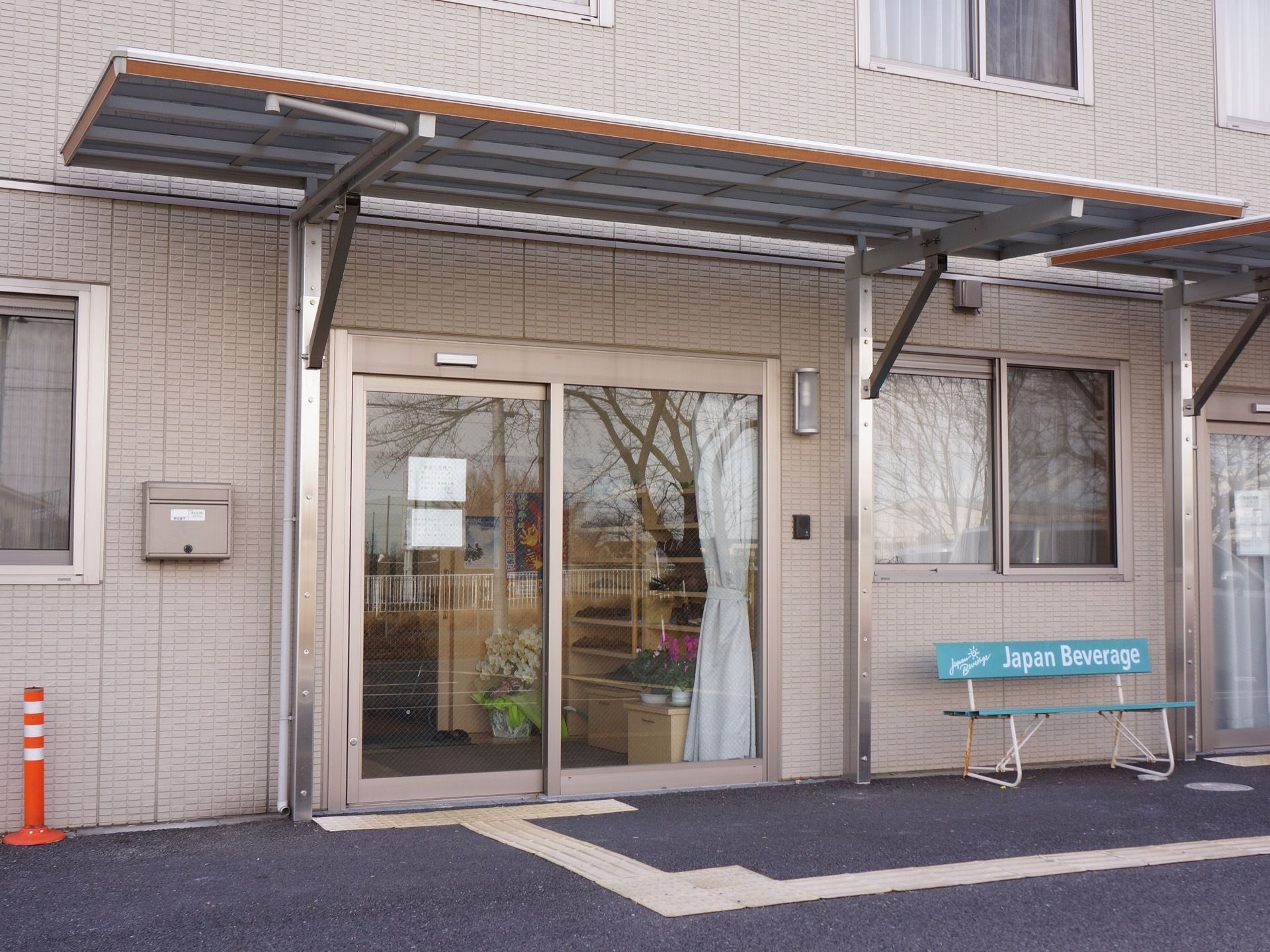 中の様子が見える自動ドアの玄関。玄関までの道には、点字ブロックが完備されている。また、玄関横にベンチがおかれている。