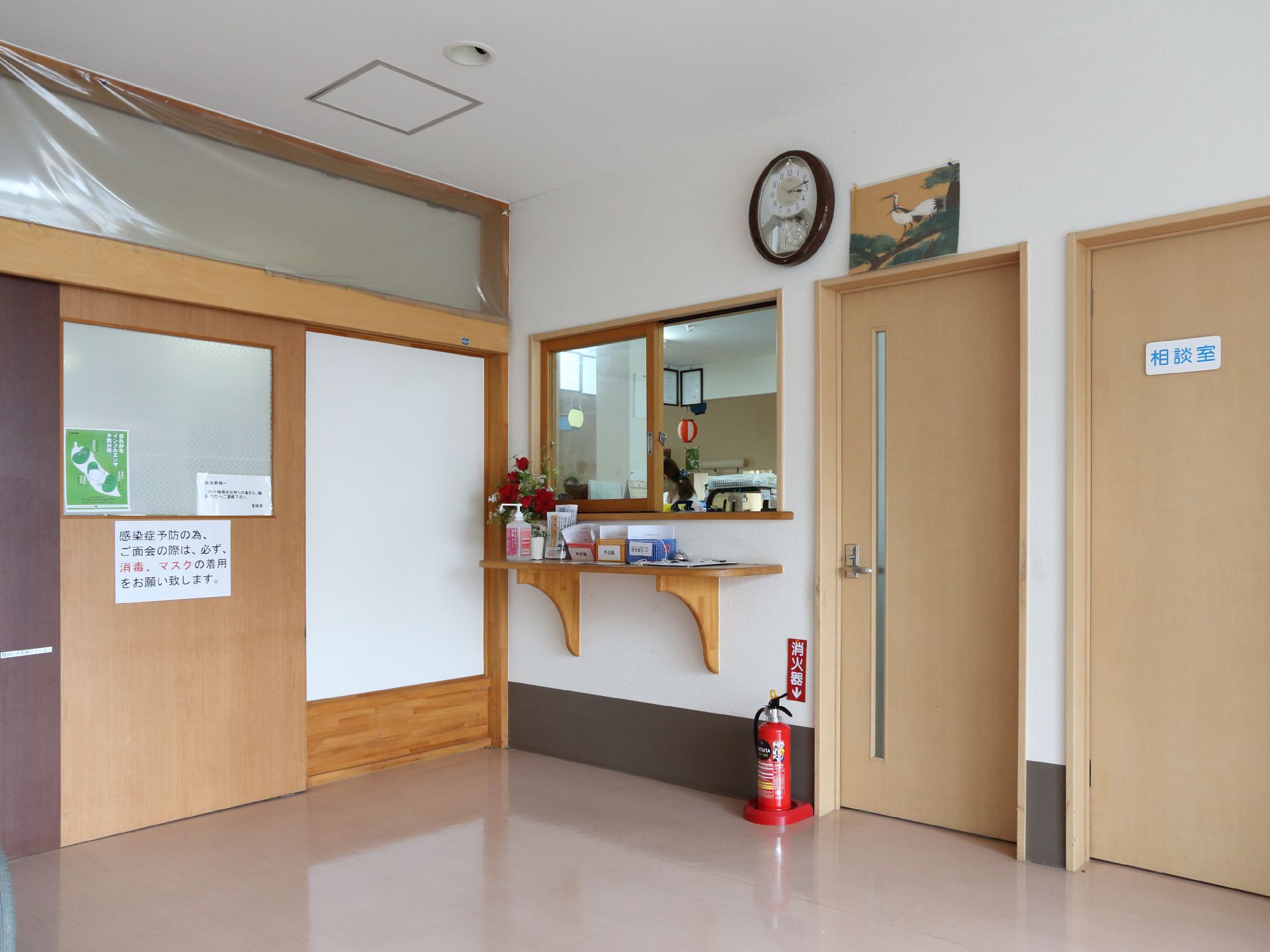 施設内には、相談室が設置されている。窓が付いた受付があり、受付の前には花飾りや消毒液が置かれている。
