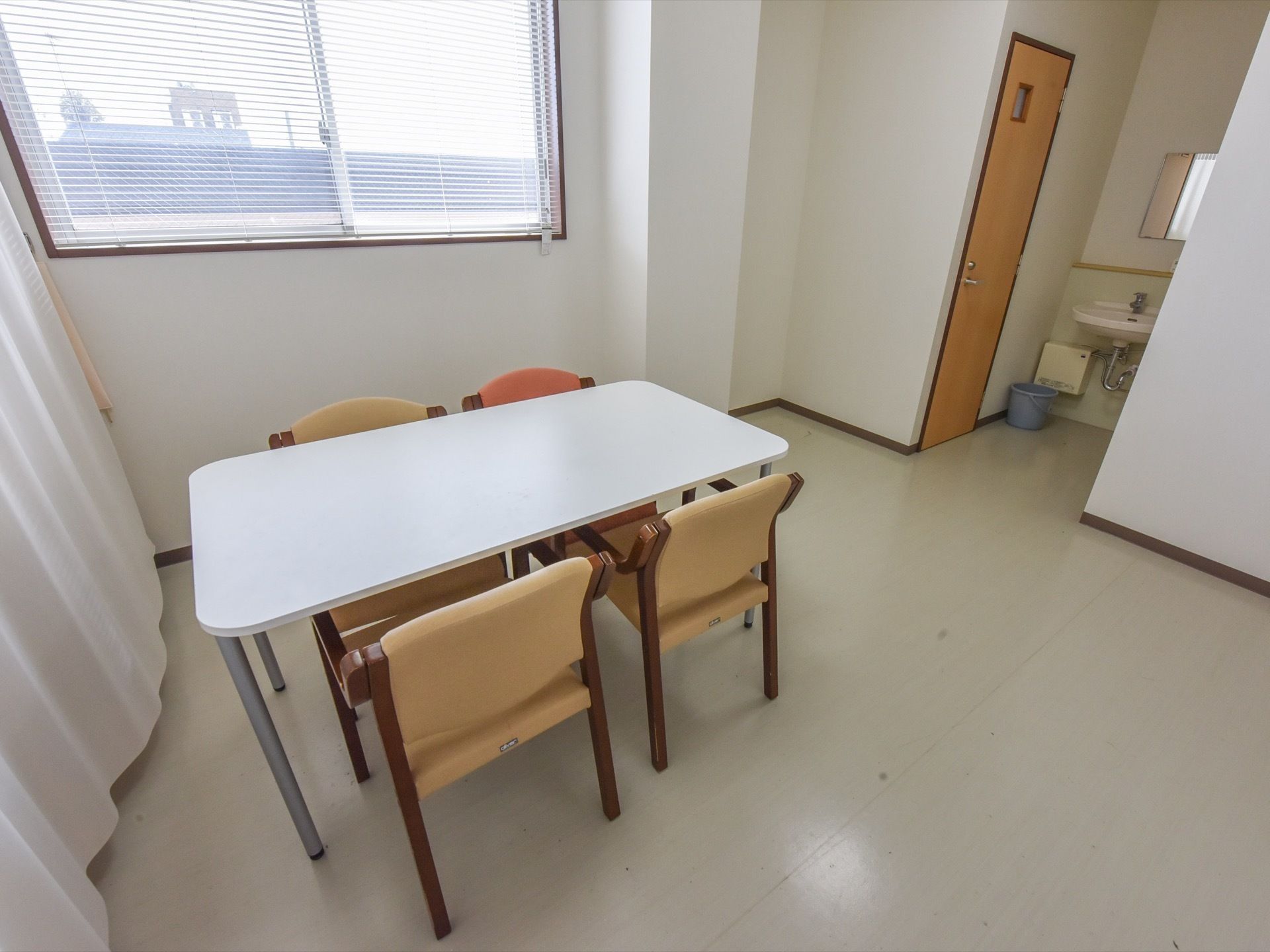 カーテンで仕切られた部屋にテーブルがあり、４脚の椅子がセットされている。部屋にはブラインドが掛けられた窓がある。