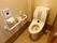 フローリングの床で、洋式トイレがある。壁に手すりがついている。水を流す場所が貯水タンクの横のほかに、壁についている。