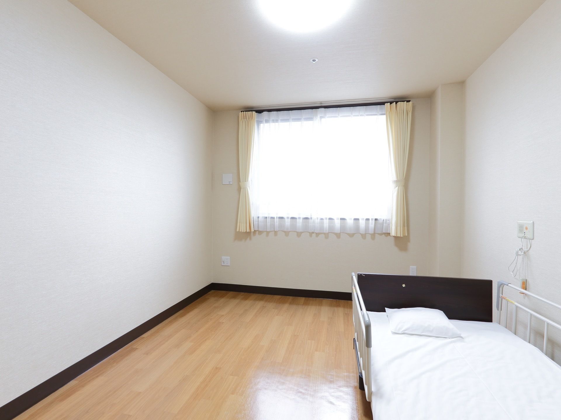 清潔感のある白が基調の日当たりの良い居室の窓には同系色のカーテンが取り付けられている。部屋全体が落ち着いた雰囲気である。