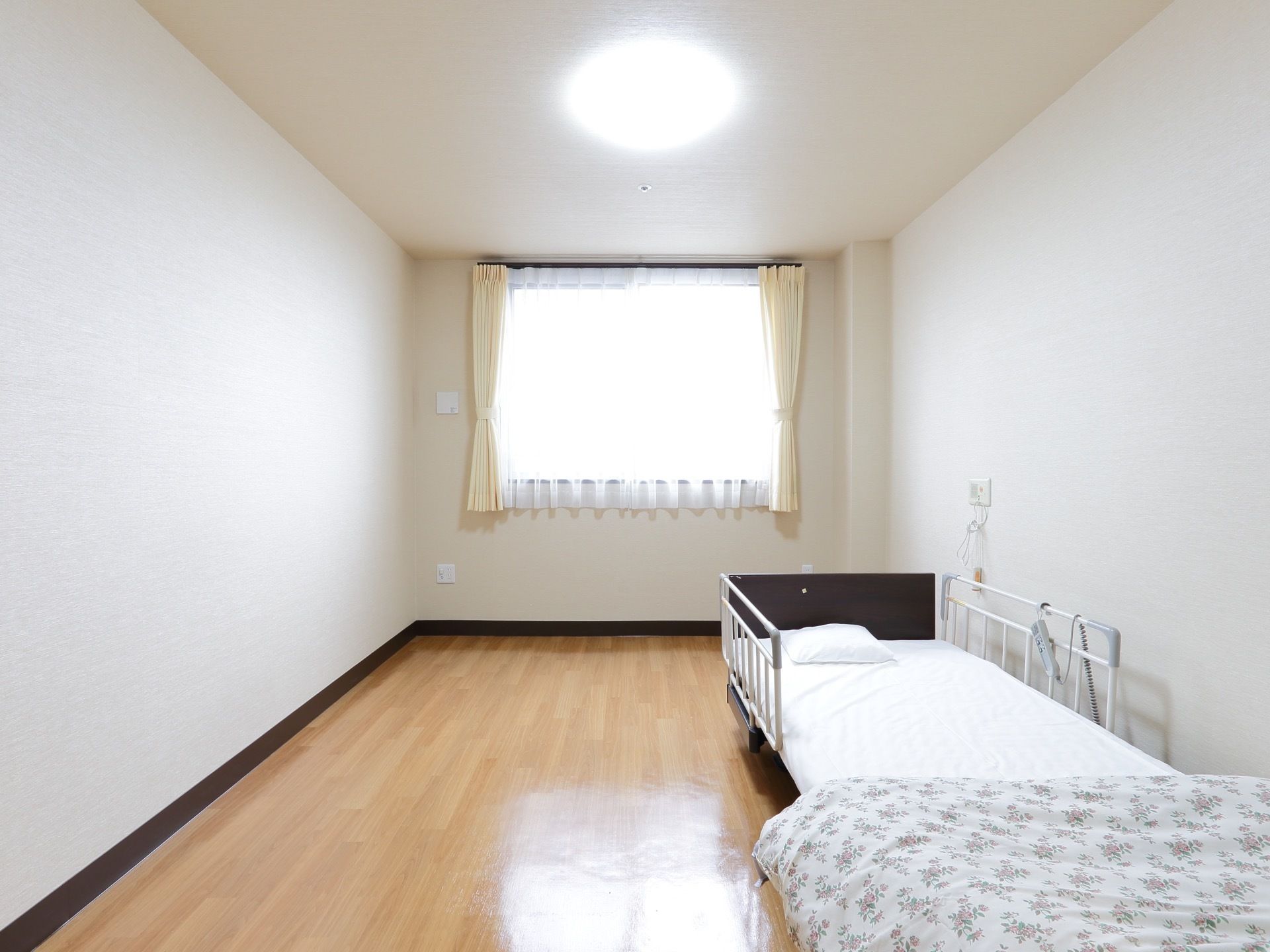 白が基調の清潔感あふれる居室には介護用ベッドと布団セットが完備されている。ＬＥＤ照明なので部屋全体が明るい。