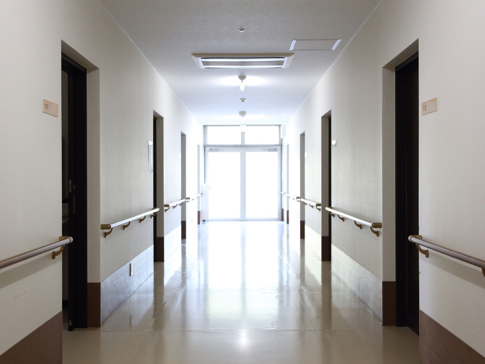 １階の廊下の様子。明るい色の木製の手すりが設置され、左右に並ぶ居室のドアの前には部屋番号の振られたプレートがある。