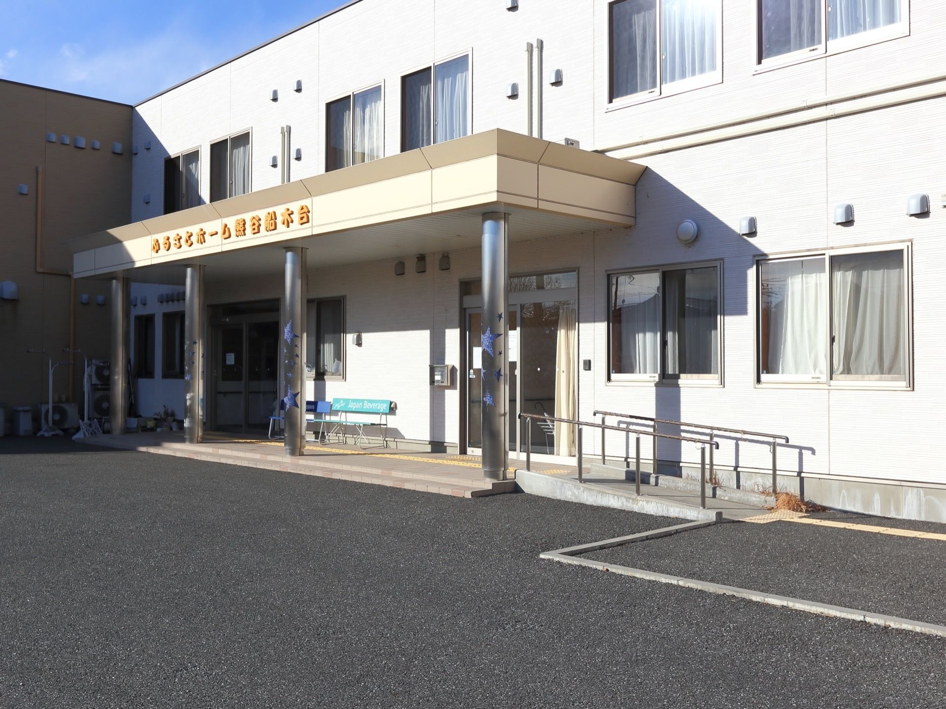 建物入口前には2段の段差がある。横に傾斜の緩やかな手すり付きのスロープがある。入口横にベンチが置かれている。