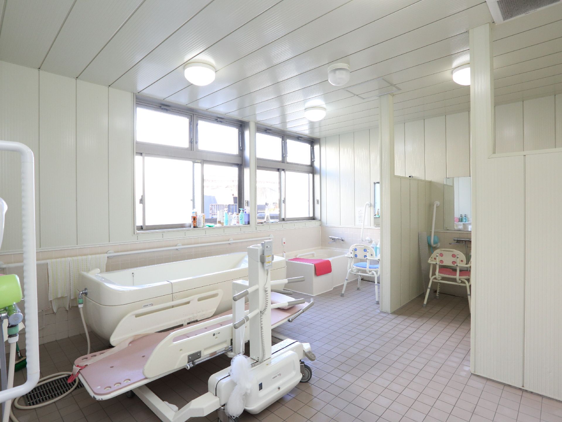 洗い場が２つある。寝た状態で浴槽に入れる機械が用意されている。浴室内は白を基調としていて、広く明るい。