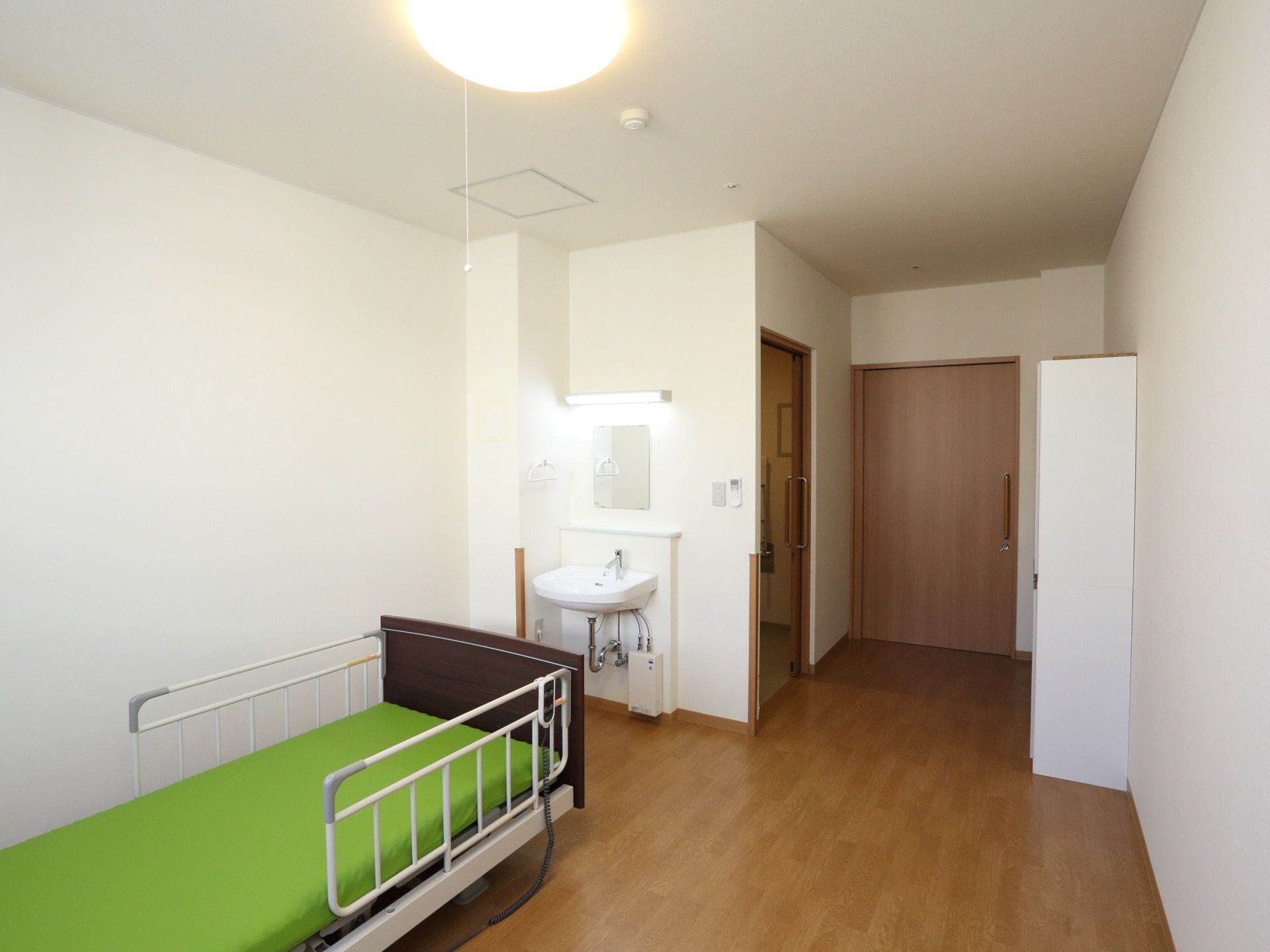部屋の扉は引戸になっている。足元はバリアフリー。落下防止柵付きのベッドの前には洗面台と鏡が設置されている。