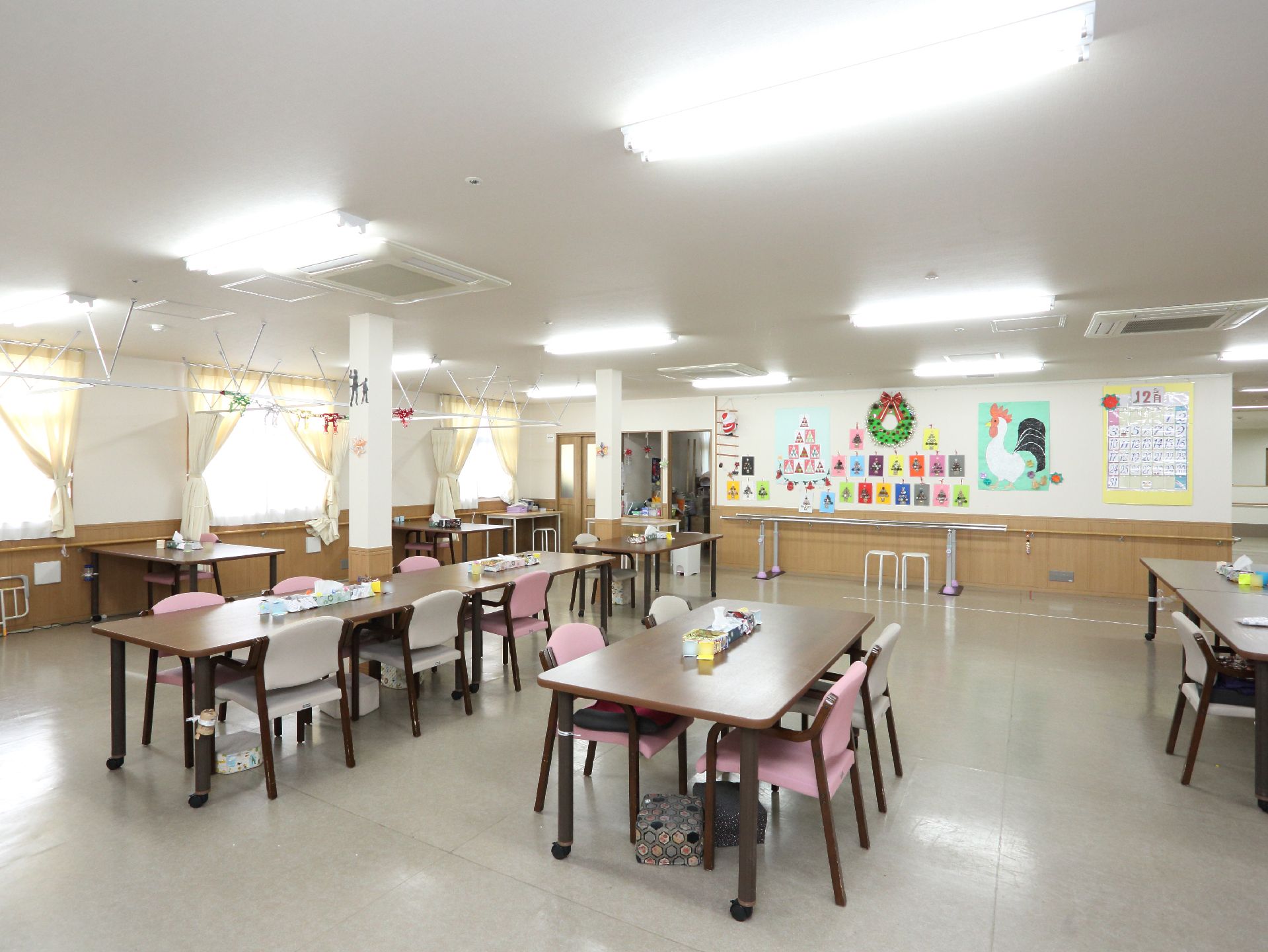 広い空間にテーブルと椅子が間隔をあけて置かれている。壁には手すりがあり、歩行訓練のバーが用意されている。
