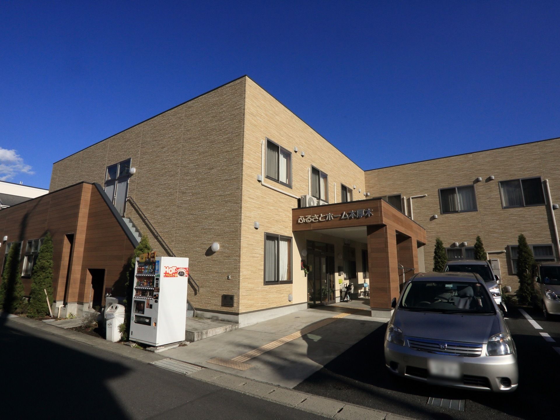 建物の横に自動販売機が設置されている。道路と敷地内には傾斜も段差も無い。駐車場が建物の目の前にある。