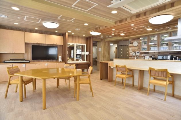 明るく開放的なダイニングキッチンである。車椅子のまま席に着けるダイニングテーブルが置かれている。壁面収納が備えつけられている。